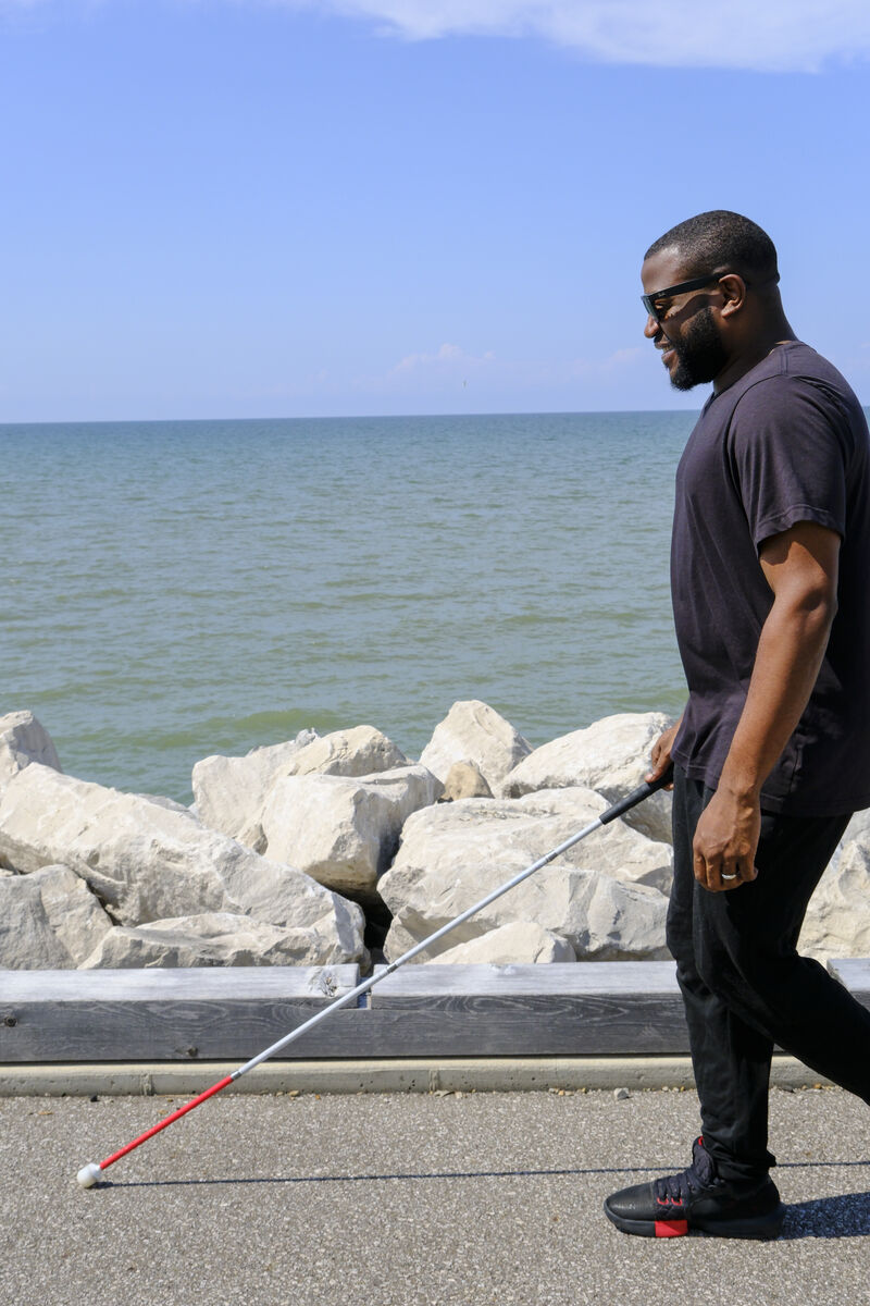 Kayshawn walks along a paved path next to Lake Erie with his white cane.