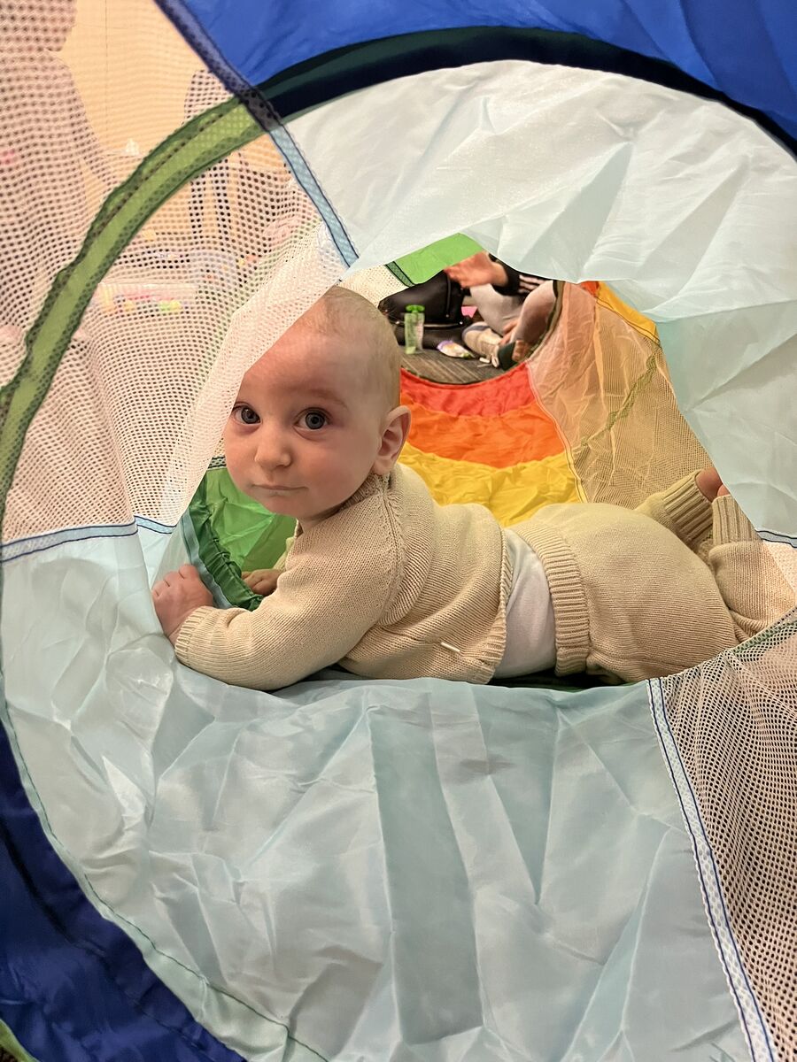 A photo of Akiva getting tummy time in a play tunnel.