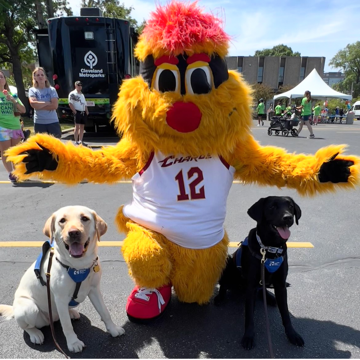 Two guide dogs in training pose for a photo with Cleveland Charge's mascot