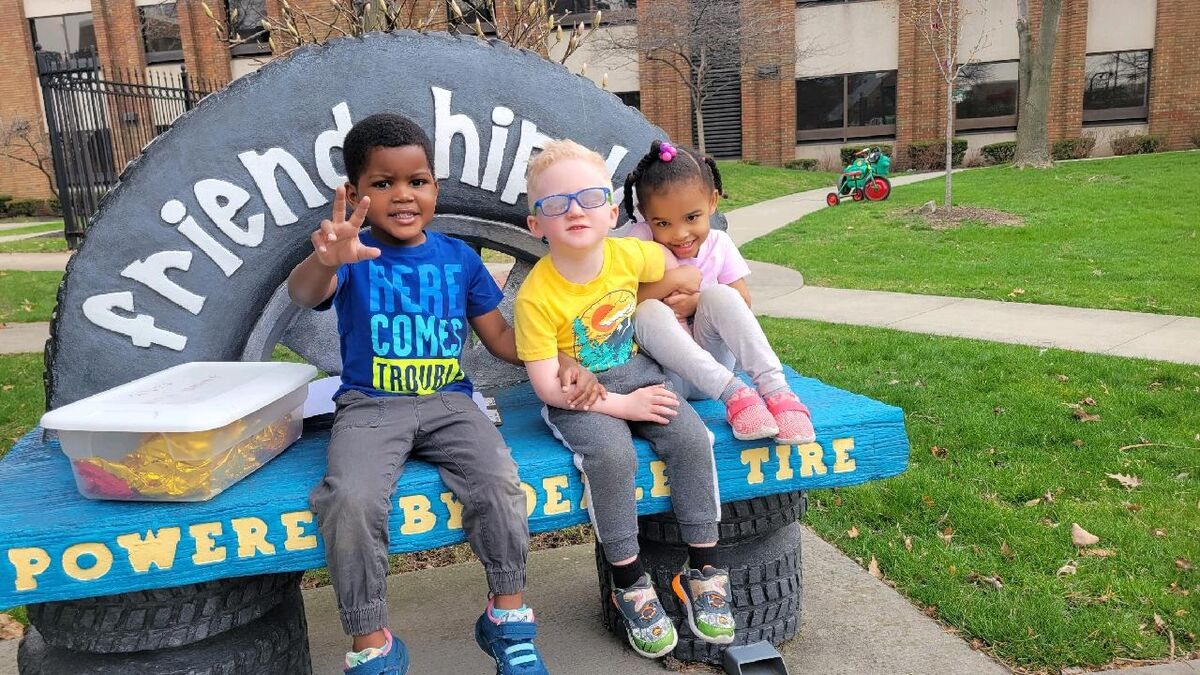 three preschoolers sit by each other on a bench in CSC's playground area